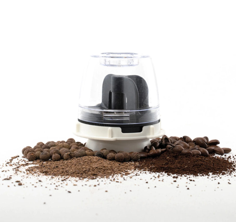 FinaPod Black Max Mahlkapsel umgeben von ganzen Kaffeebohnen und Pimentkörnern sowie dem frisch gemahlenen Ergebnis