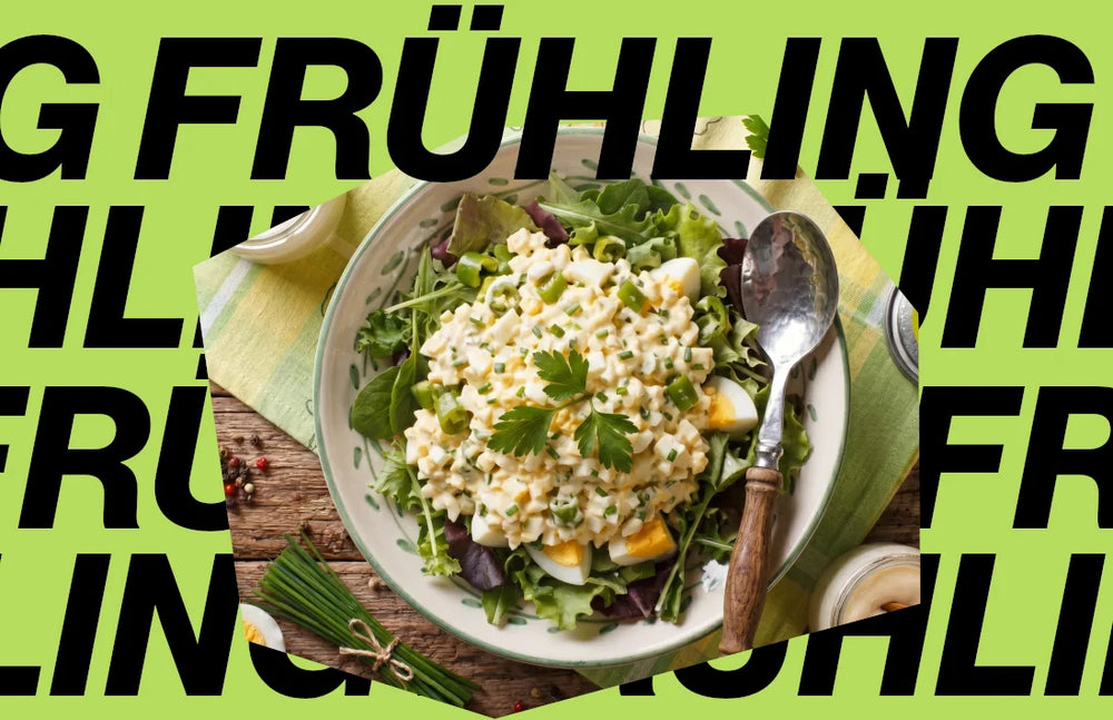Eine Schüssel mit frischem, fein gehacktem Eiersalat und Frühlingskräutern, angerichtet auf einem Holztisch vor einem markanten Frühlings-Schriftzug
