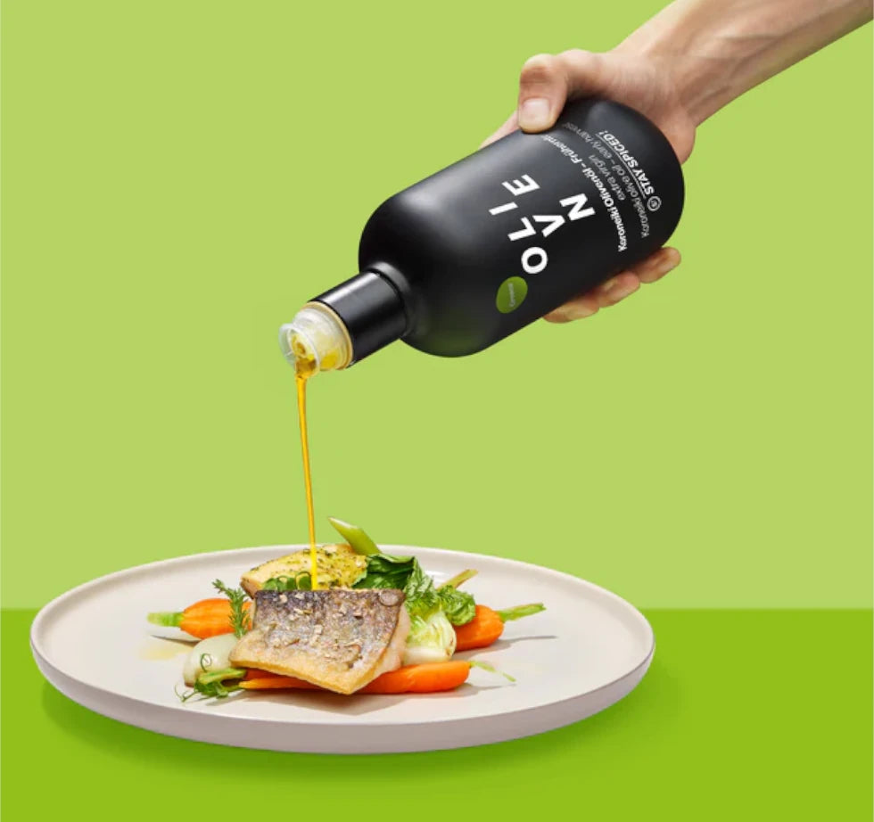 Extra Natives STAY SPICED! Olivenöl Frühernte wird aus der schwarzen Flasche über ein feines Fischgericht gegossen