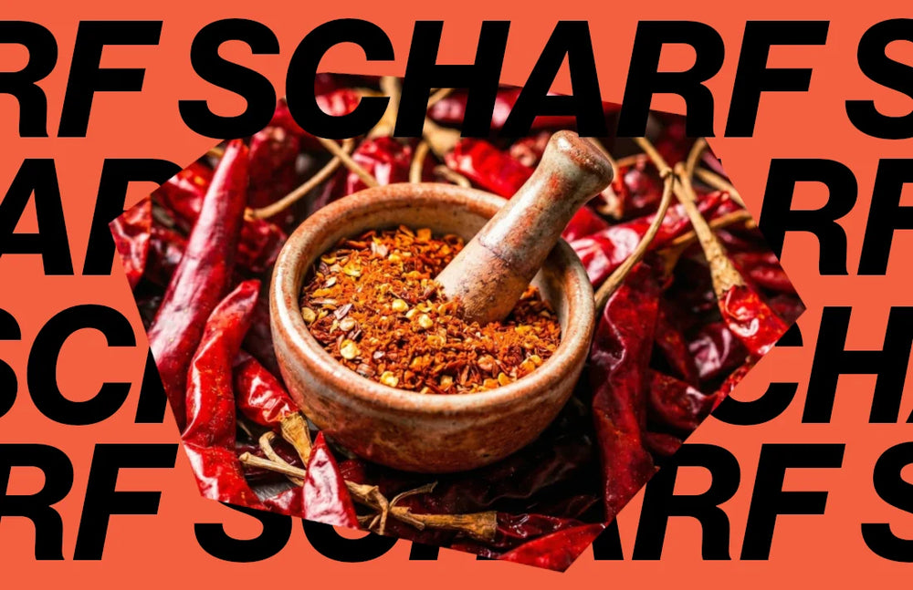 Ein hölzerner Mörser gefüllt mit gemahlenem Chilipulver, umgeben von getrockneten ganzen Chilis, ideal für die individuelle Dosierung von Schärfe