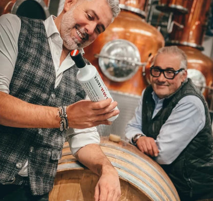 Roland Trettl und Hans Reisetbauer präsentieren stolz ihre handgefertigte Bio-Soja Sauce vor Holzfässern in der traditionellen Qualitätsbrennerei