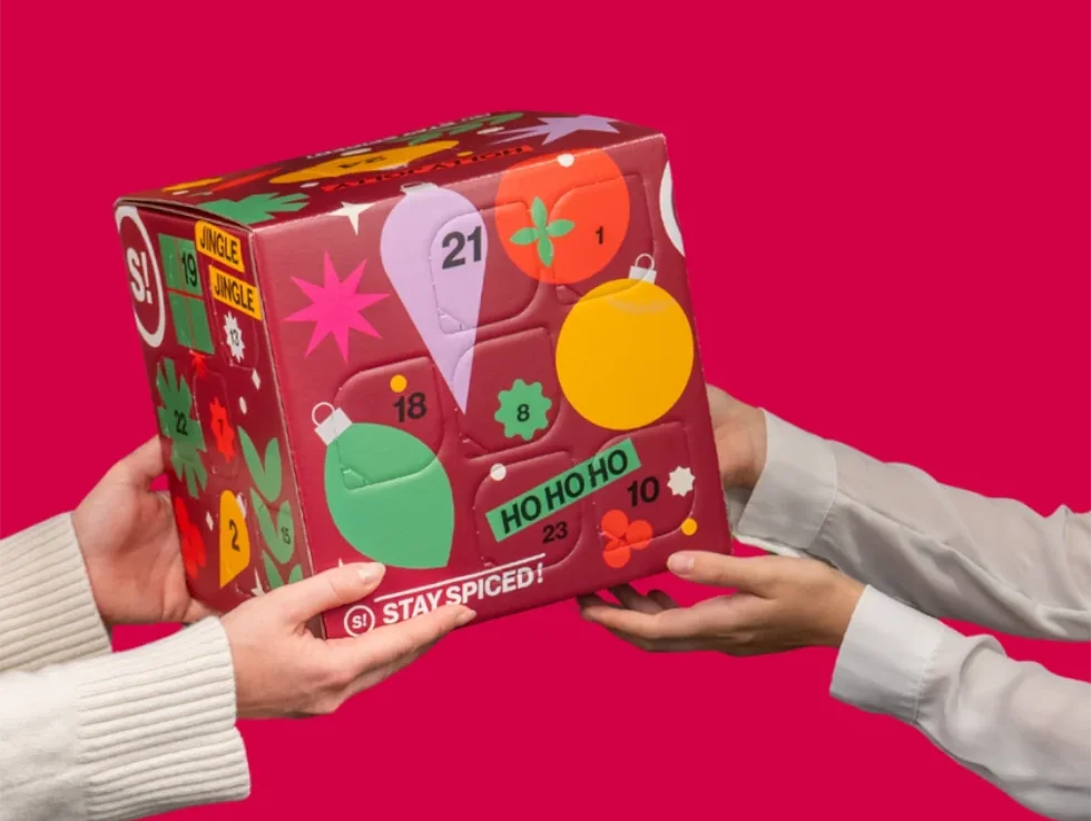 Zwei Hände präsentieren den roten STAY SPICED! Gewürz-Adventskalender 2026 in der Edition Spice Cube Deluxe von Chefkoch-Gewürze