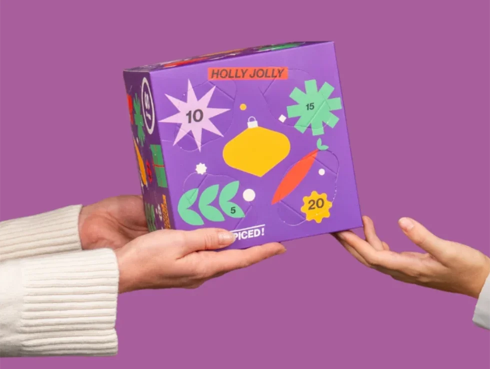 Zwei Hände halten den lilafarbenen STAY SPICED! Gewürz-Adventskalender 2026 in der Edition Spice Cube Mini von Chefkoch-Gewürze.