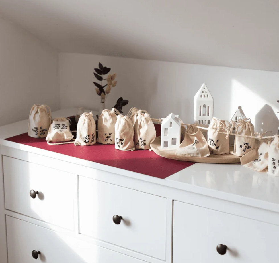 Die 24 nummerierten Jutesaeckchen des STAY SPICED! DIY Adventskalenders als festliche Weihnachtsgirlande auf einer Kommode dekoriert